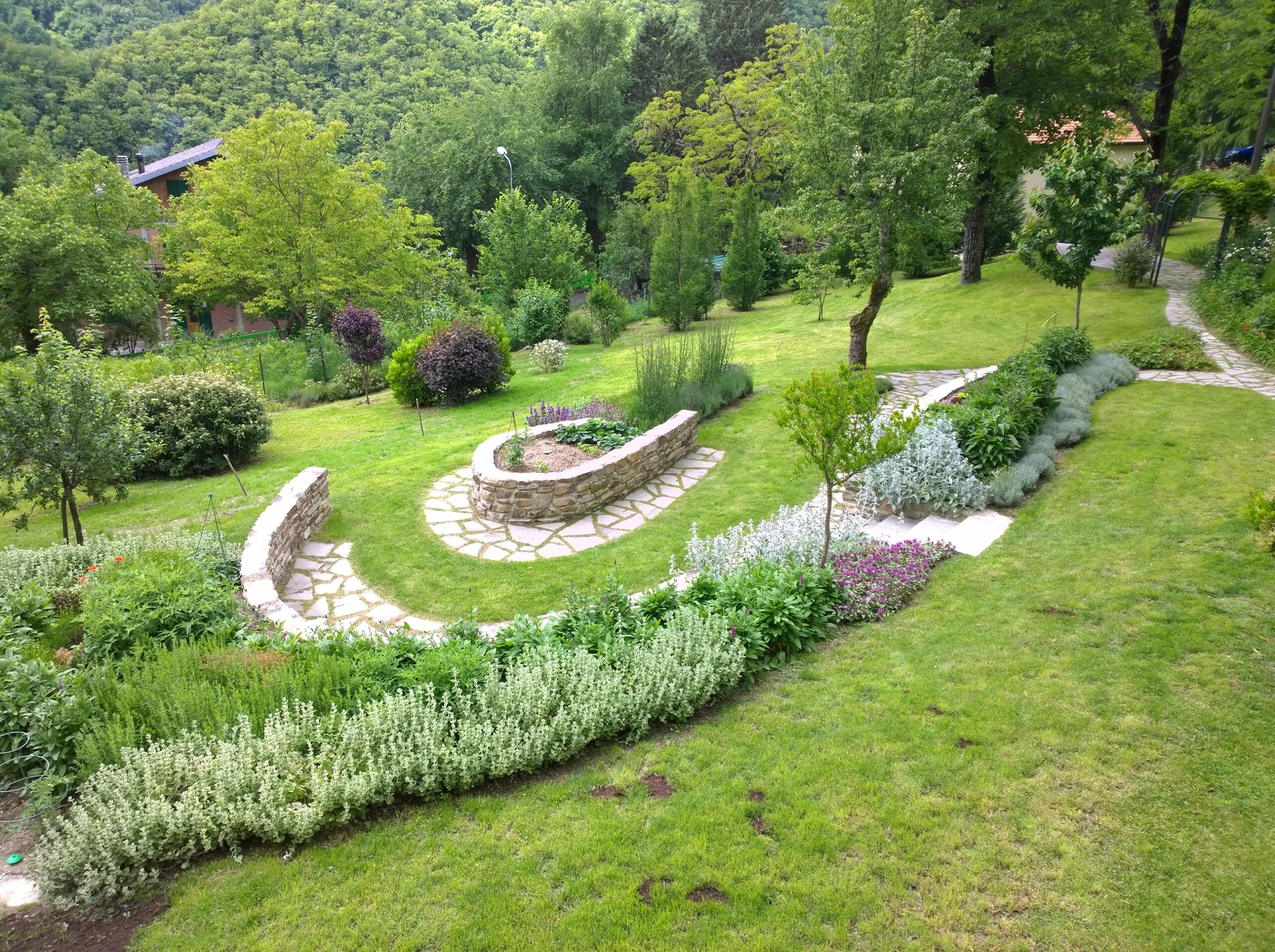 Giardino realizzato con percorsi in pietra, muretti curvi e aiuole integrate nel paesaggio